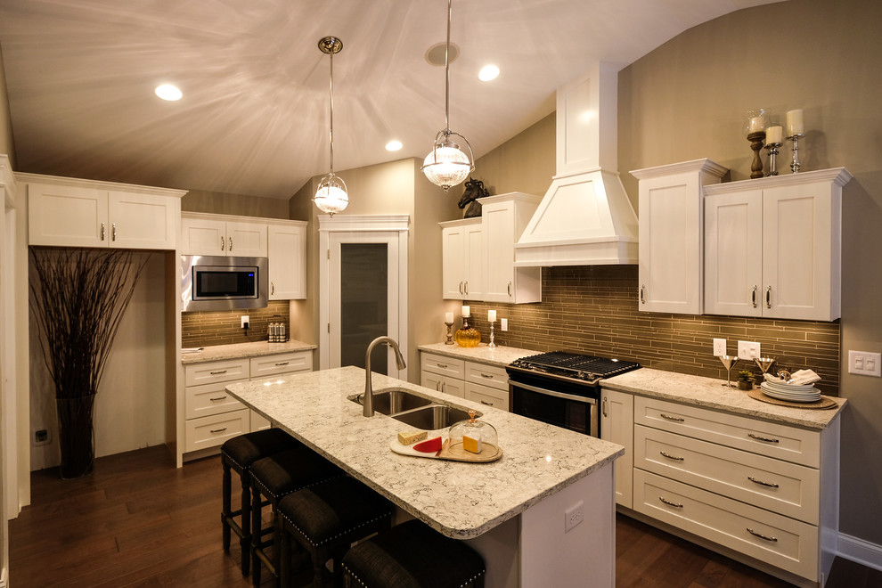 Example of a mid-sized transitional l-shaped dark wood floor and brown floor eat-in kitchen design with an undermount sink, recessed-panel cabinets, white cabinets, quartz countertops, brown backsplash, stainless steel appliances, an island and white countertops