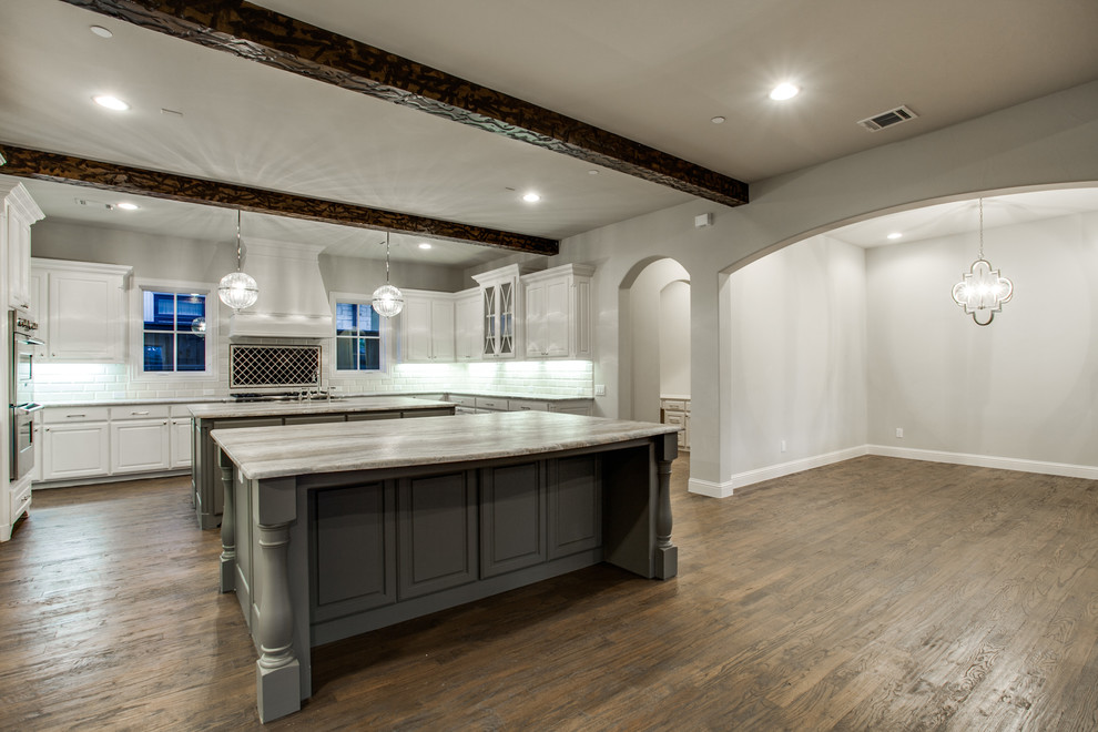 Inspiration for a large traditional u-shaped eat-in kitchen in Dallas with a farmhouse sink, flat-panel cabinets, white cabinets, limestone benchtops, white splashback, cement tile splashback, stainless steel appliances, dark hardwood floors and multiple islands.