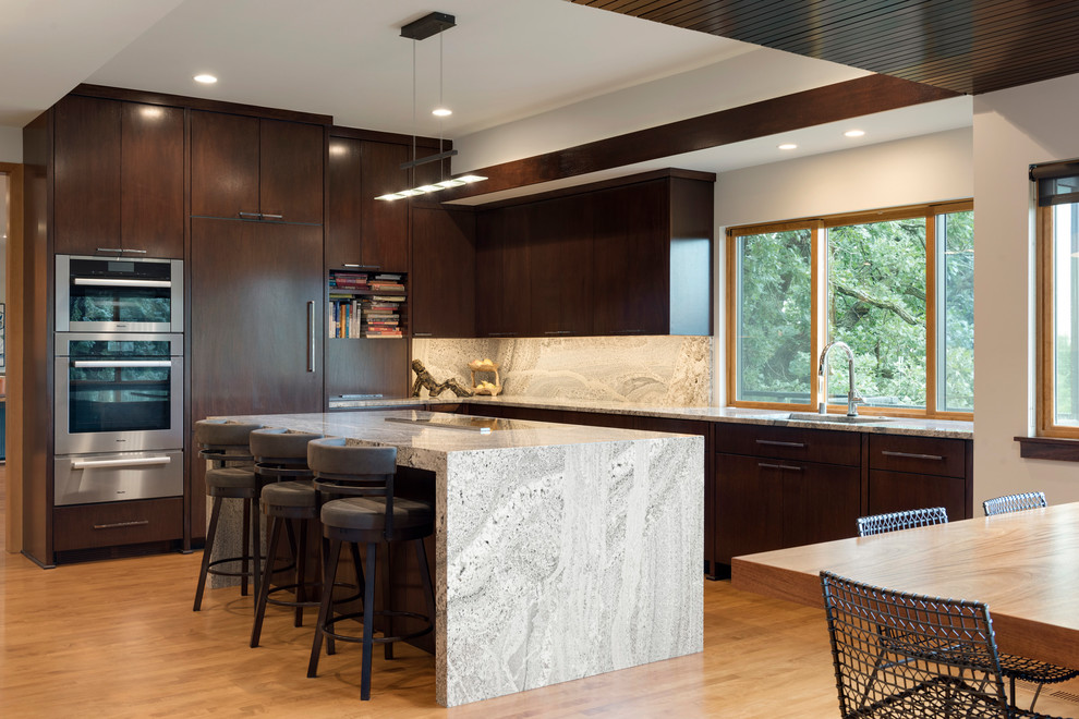 Design ideas for a midcentury l-shaped eat-in kitchen in Minneapolis with a single-bowl sink, flat-panel cabinets, dark wood cabinets, grey splashback, panelled appliances, light hardwood floors, with island and grey benchtop.