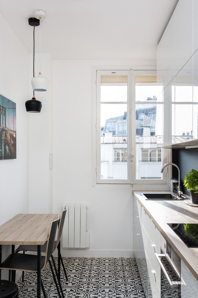 Inspiration for a mid-sized contemporary single-wall separate kitchen in Paris with wood benchtops, no island, a drop-in sink, flat-panel cabinets, white cabinets, black splashback, slate splashback, stainless steel appliances, cement tiles, multi-coloured floor and beige benchtop.
