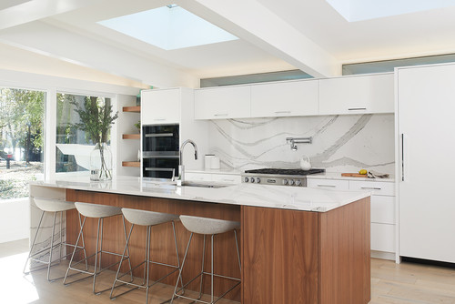 Bright modern kitchen with white RTA cabinets, walnut waterfall island, marble-look backsplash, skylights, and four bar stools.