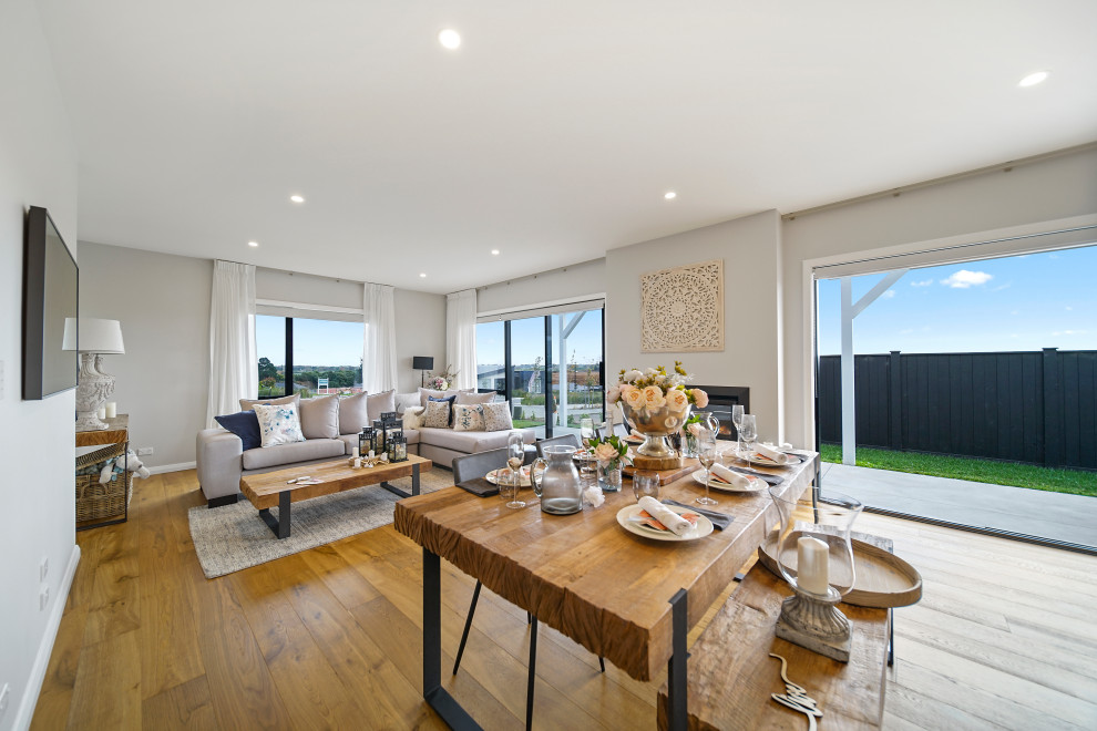 Large country kitchen/dining combo in Auckland with white walls, medium hardwood floors, a hanging fireplace, a tile fireplace surround, brown floor and vaulted.