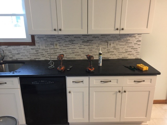 Mid-sized transitional l-shaped eat-in kitchen photo in Columbus with an undermount sink, shaker cabinets, white cabinets, granite countertops, white backsplash, glass tile backsplash, black appliances and an island