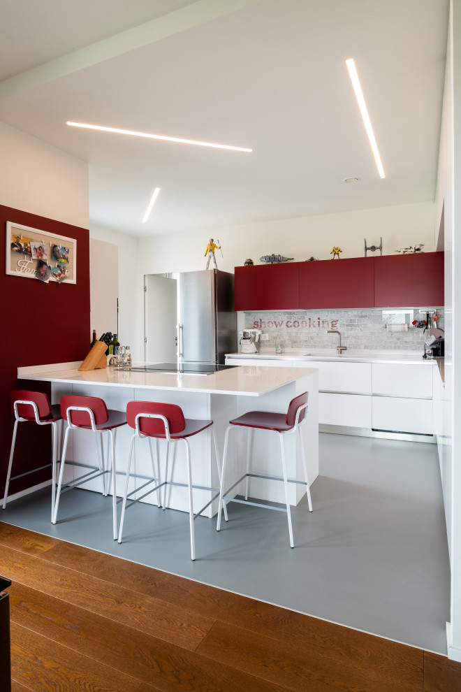 Idéer för ett modernt vit l-kök, med en undermonterad diskho, släta luckor, röda skåp, grått stänkskydd, rostfria vitvaror, en halv köksö och grått golv