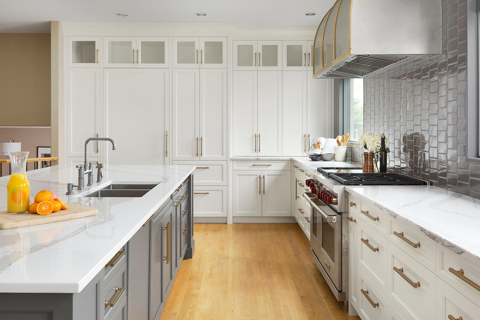 Example of a large transitional single-wall light wood floor and brown floor open concept kitchen design in Calgary with an undermount sink, shaker cabinets, white cabinets, marble countertops, gray backsplash, ceramic backsplash, stainless steel appliances and an island