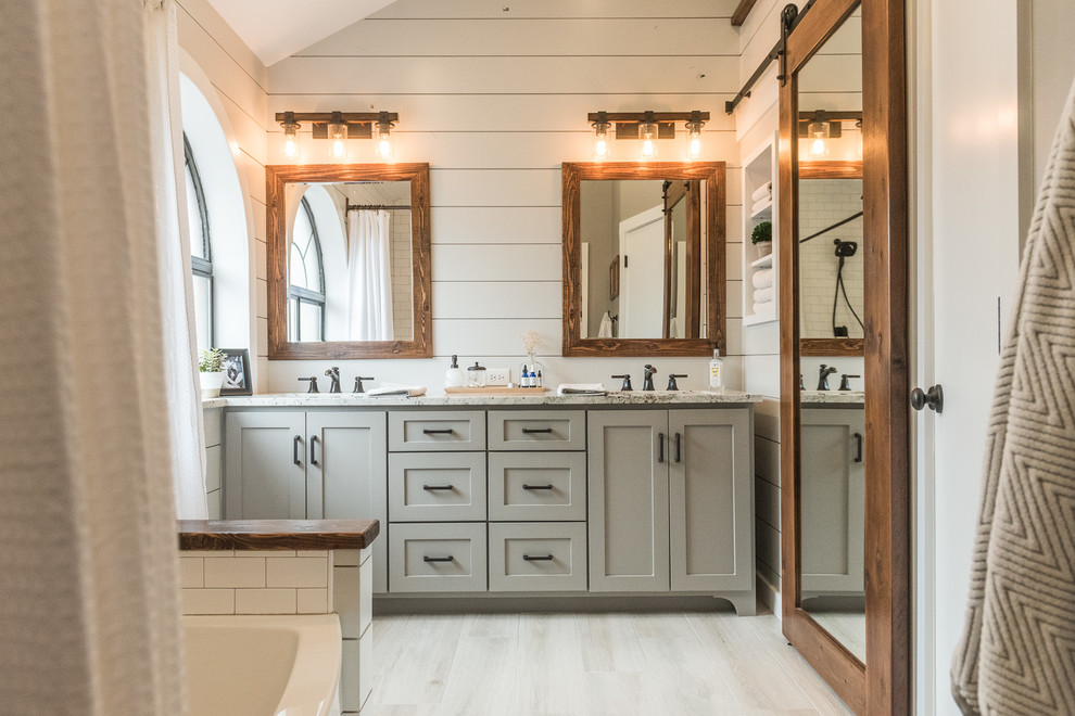 Photo of a mid-sized country master bathroom in Dallas with shaker cabinets, grey cabinets, an alcove tub, a shower/bathtub combo, a one-piece toilet, gray tile, porcelain tile, grey walls, porcelain floors, an undermount sink and granite benchtops.