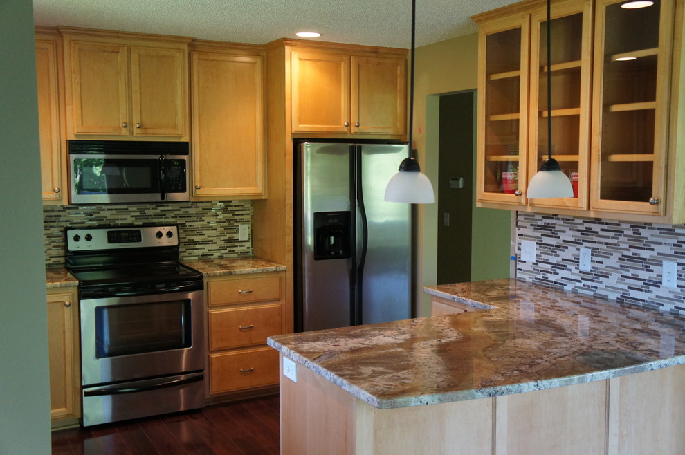 Inspiration for a mid-sized timeless brown floor and laminate floor enclosed kitchen remodel in Minneapolis with a double-bowl sink, recessed-panel cabinets, light wood cabinets, granite countertops, brown backsplash, glass tile backsplash, stainless steel appliances and a peninsula