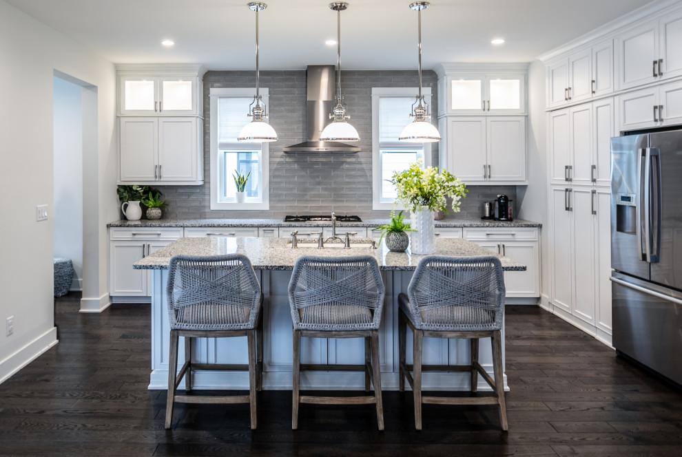 Transitional l-shaped kitchen in Detroit with an undermount sink, recessed-panel cabinets, white cabinets, grey splashback, subway tile splashback, stainless steel appliances, dark hardwood floors, with island, brown floor and grey benchtop.