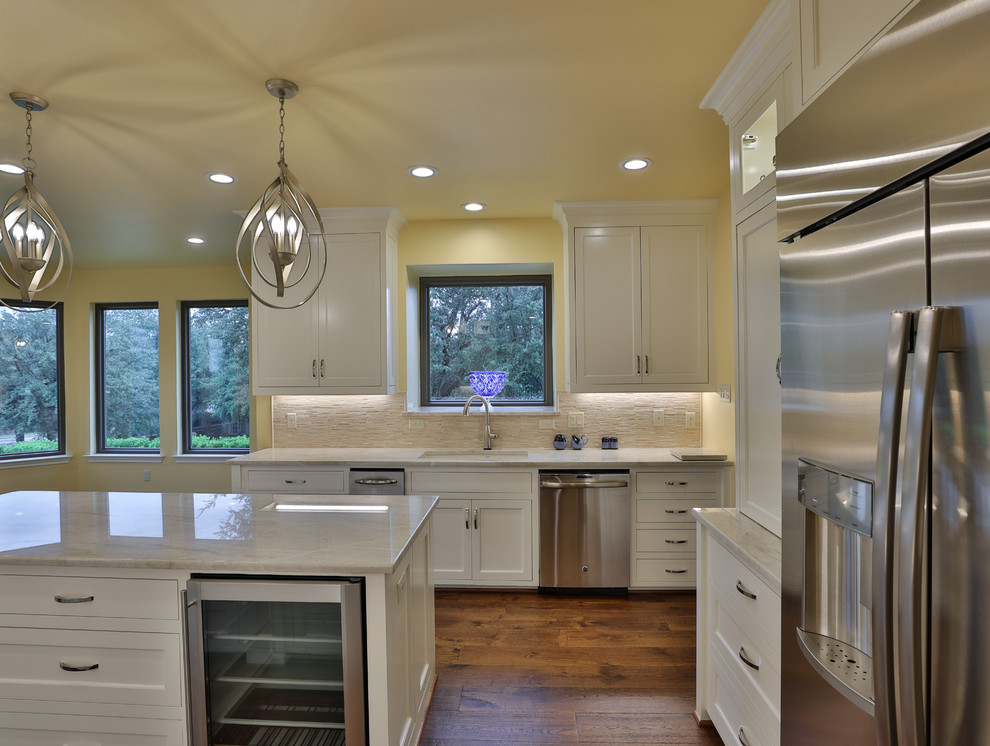 Design ideas for a transitional kitchen in Dallas with an undermount sink, recessed-panel cabinets, white cabinets, quartzite benchtops, beige splashback, stone tile splashback, stainless steel appliances, dark hardwood floors, with island, brown floor and beige benchtop.