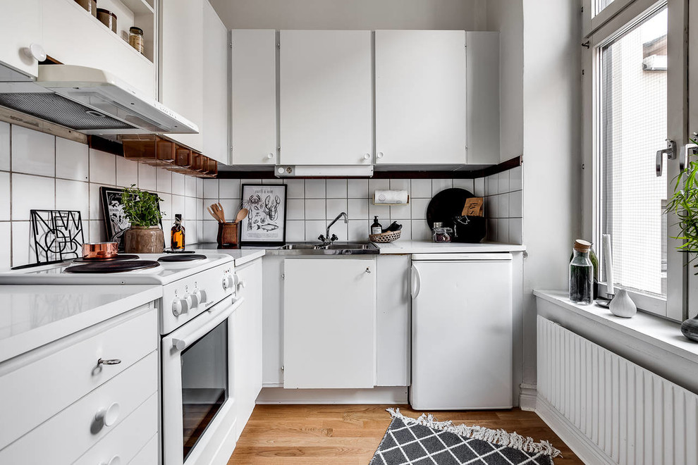 Inspiration for a small scandinavian l-shaped separate kitchen in Stockholm with a drop-in sink, flat-panel cabinets, white cabinets, white splashback, white appliances, medium hardwood floors, no island and brown floor.