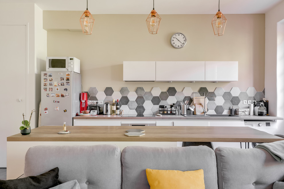 Design ideas for a mid-sized transitional single-wall open plan kitchen in Lyon with an undermount sink, flat-panel cabinets, white cabinets, laminate benchtops, grey splashback, ceramic splashback, white appliances, laminate floors, with island, grey floor and brown benchtop.