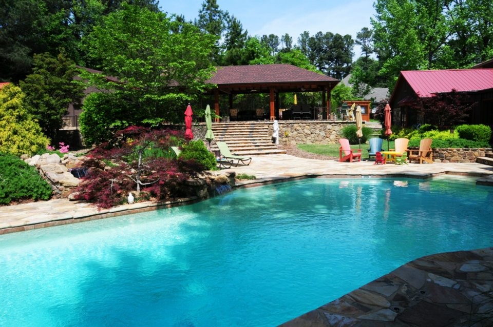 This is an example of a mid-sized transitional backyard custom-shaped pool in Other with natural stone pavers.