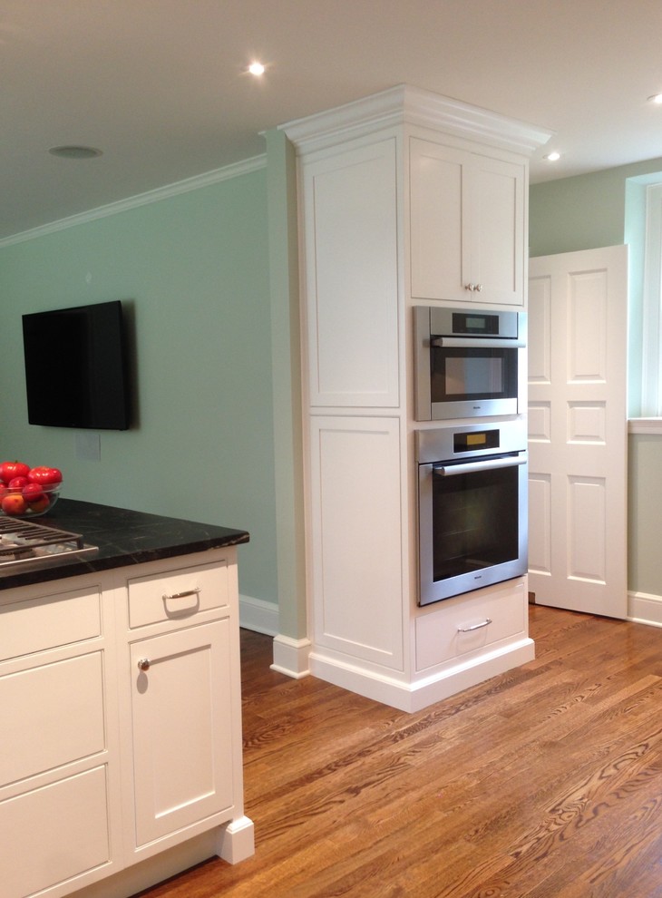 Large traditional l-shaped open plan kitchen in Philadelphia with a farmhouse sink, shaker cabinets, white cabinets, soapstone benchtops, stainless steel appliances, medium hardwood floors and a peninsula.