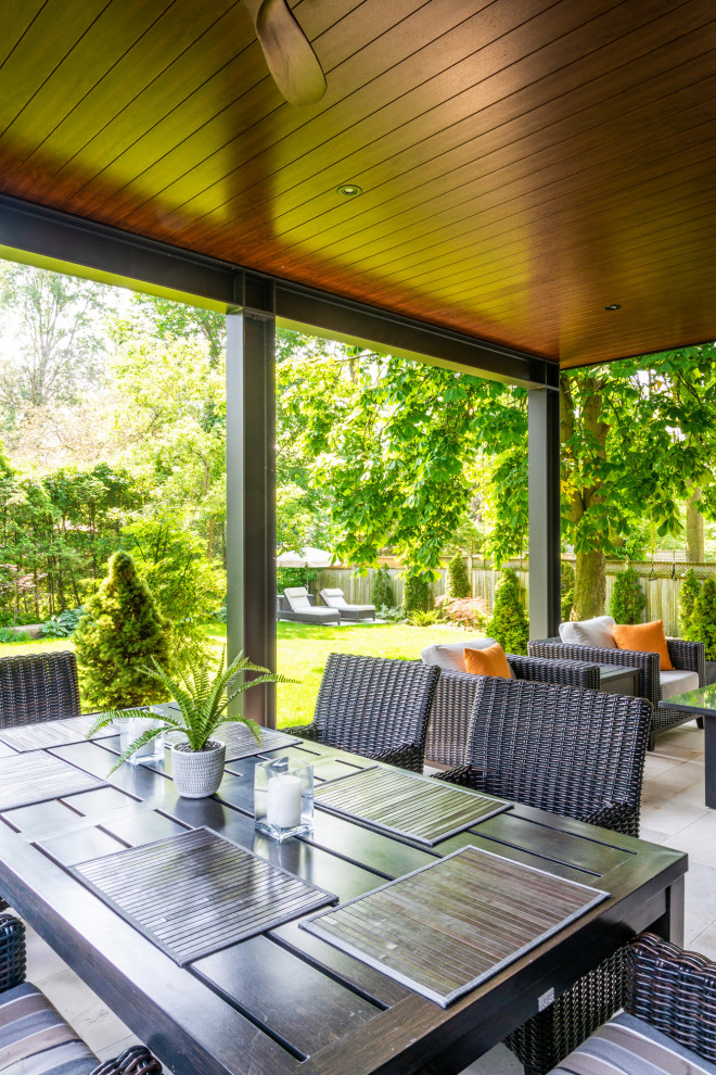 Idée de décoration pour une grande terrasse arrière minimaliste avec des pavés en pierre naturelle et une extension de toiture.