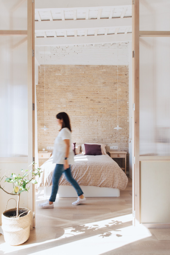 Foto di una piccola camera matrimoniale industriale con pareti bianche, pavimento in laminato, travi a vista e pareti in mattoni