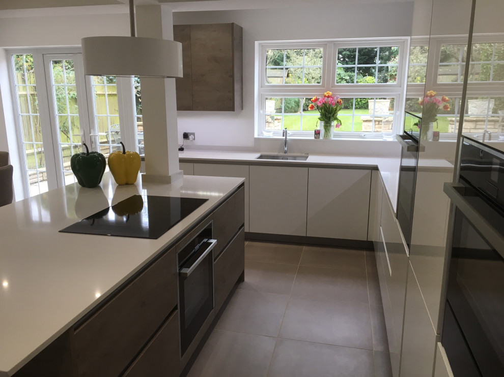 This is an example of a mid-sized contemporary l-shaped open plan kitchen in Hertfordshire with an undermount sink, flat-panel cabinets, white cabinets, quartzite benchtops, white splashback, porcelain floors, with island, brown floor, white benchtop and recessed.