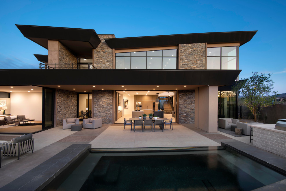 Exemple d'une très grande terrasse arrière moderne avec un foyer extérieur, des pavés en pierre naturelle et une extension de toiture.