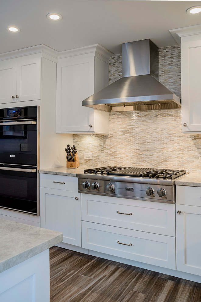 Inspiration for a large transitional galley porcelain tile eat-in kitchen remodel in Chicago with a farmhouse sink, shaker cabinets, white cabinets, quartzite countertops, multicolored backsplash, glass sheet backsplash, stainless steel appliances and an island