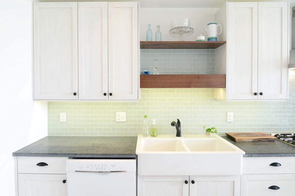 This is an example of a mid-sized midcentury galley eat-in kitchen in Philadelphia with a farmhouse sink, shaker cabinets, white cabinets, blue splashback, subway tile splashback, stainless steel appliances, porcelain floors, a peninsula, beige floor, granite benchtops and black benchtop.