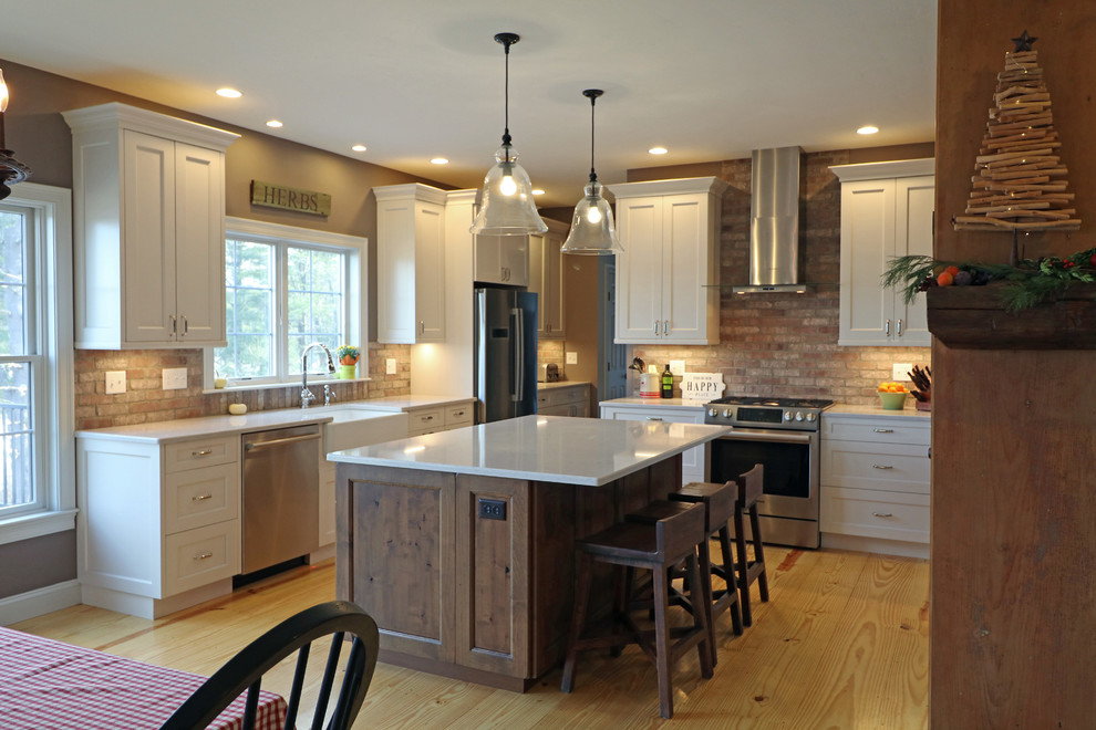 This is an example of a mid-sized country l-shaped eat-in kitchen in Boston with a farmhouse sink, shaker cabinets, white cabinets, quartz benchtops, brown splashback, brick splashback, stainless steel appliances, medium hardwood floors, with island and yellow floor.