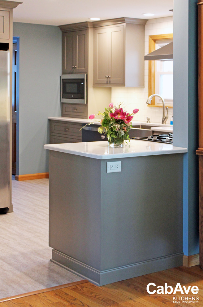 Inspiration for a small transitional l-shaped laminate floor and gray floor enclosed kitchen remodel with a farmhouse sink, recessed-panel cabinets, gray cabinets, quartz countertops, white backsplash, subway tile backsplash, stainless steel appliances and a peninsula