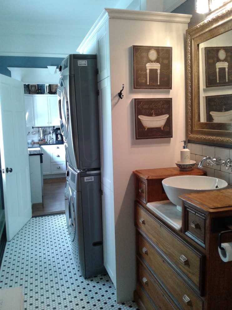 Photo of a small country single-wall utility room in Other with a single-bowl sink, beaded inset cabinets, white cabinets, wood benchtops, grey walls, a stacked washer and dryer and brown benchtop.