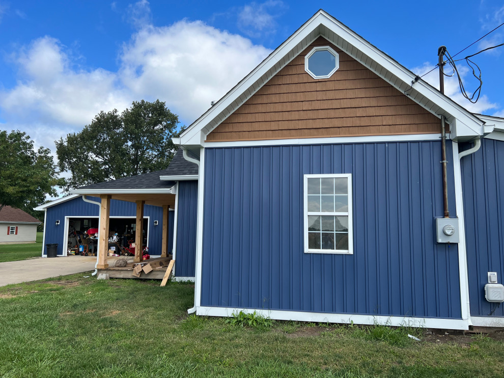 Esempio della villa grande blu country a due piani con rivestimento in vinile, pannelli e listelle di legno, copertura a scandole e tetto nero