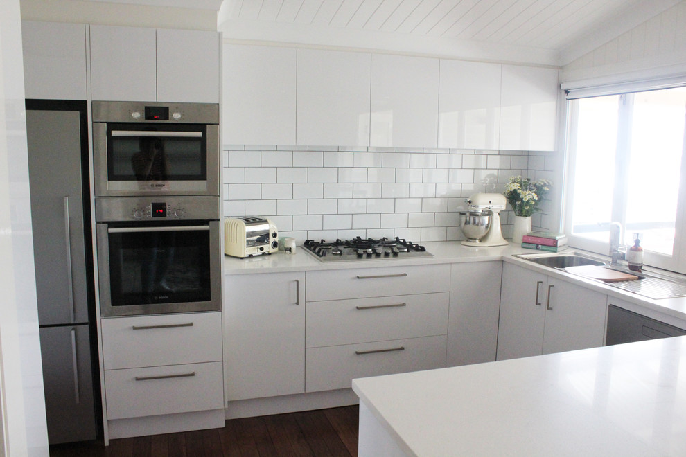 Photo of a contemporary eat-in kitchen in Brisbane with a drop-in sink, flat-panel cabinets, white cabinets, quartz benchtops, white splashback, subway tile splashback, stainless steel appliances, medium hardwood floors and with island.