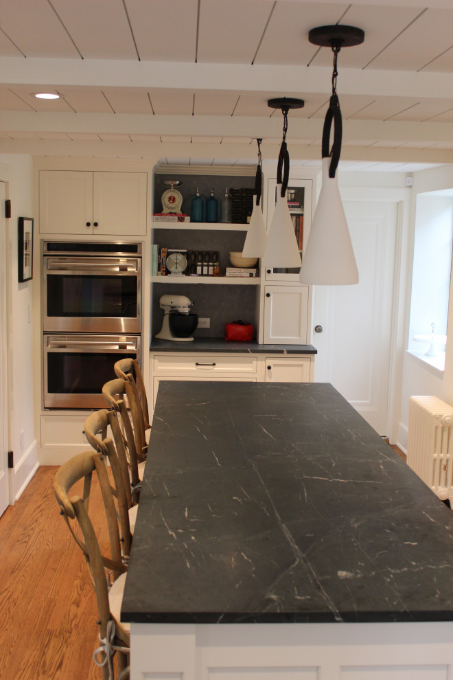 Foto på ett stort vintage grå kök, med en undermonterad diskho, luckor med infälld panel, vita skåp, bänkskiva i täljsten, vitt stänkskydd, stänkskydd i cementkakel, integrerade vitvaror, ljust trägolv, en köksö och brunt golv