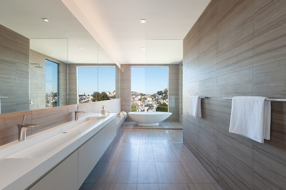 This is an example of a mid-sized modern master bathroom in San Francisco with a trough sink, flat-panel cabinets, beige cabinets, solid surface benchtops, a freestanding tub, an open shower, gray tile, stone tile, white walls, marble floors and an open shower.