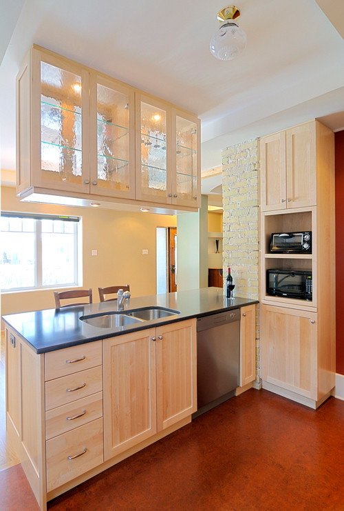 Modern inredning av ett litet kök, med en dubbel diskho, skåp i shakerstil, skåp i ljust trä, bänkskiva i kvarts, rött stänkskydd, rostfria vitvaror, korkgolv och en halv köksö