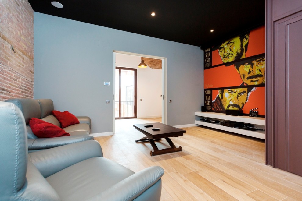 This is an example of a mid-sized industrial enclosed home theatre in Barcelona with multi-coloured walls, medium hardwood floors and a projector screen.