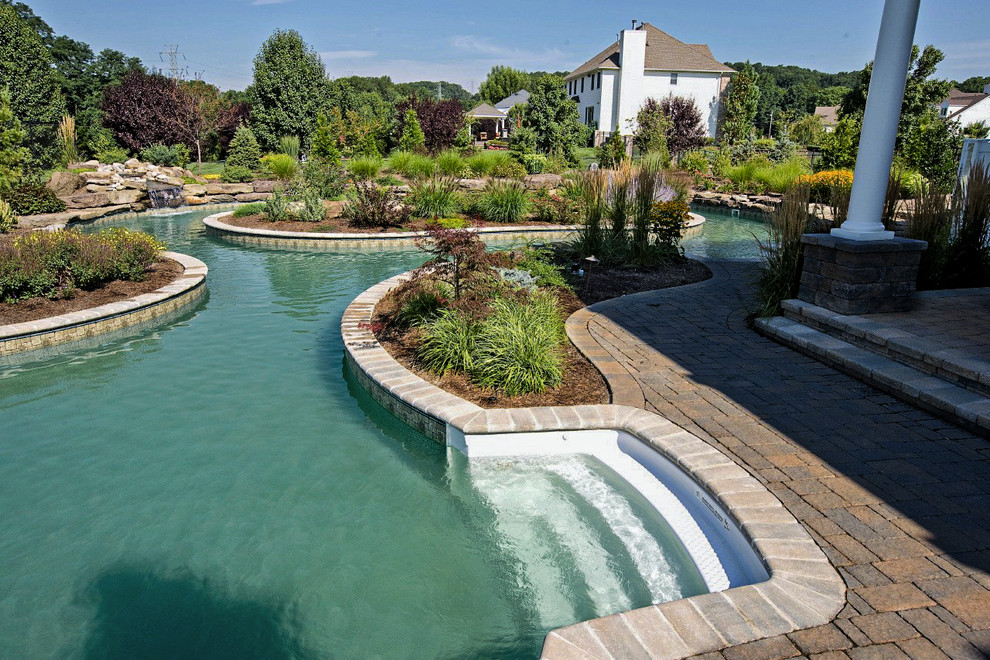 This is an example of a large contemporary backyard custom-shaped natural pool in New York with brick pavers.