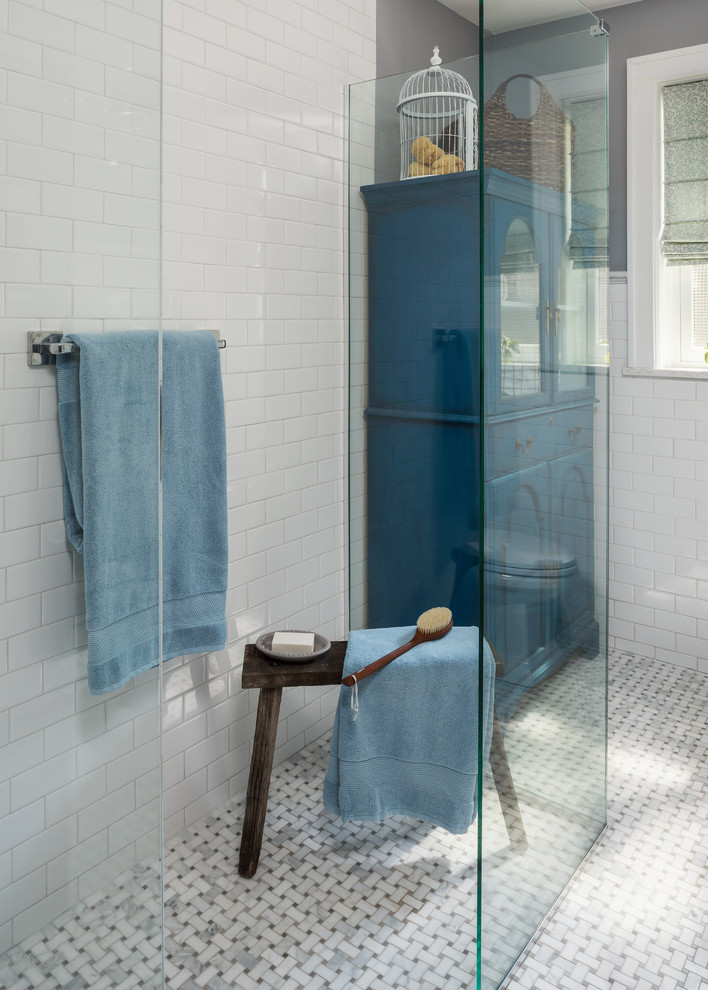 This is an example of a small traditional bathroom in St Louis with glass-front cabinets, blue cabinets, a curbless shower, a two-piece toilet, white tile, ceramic tile, grey walls, marble floors, a pedestal sink, grey floor and a sliding shower screen.