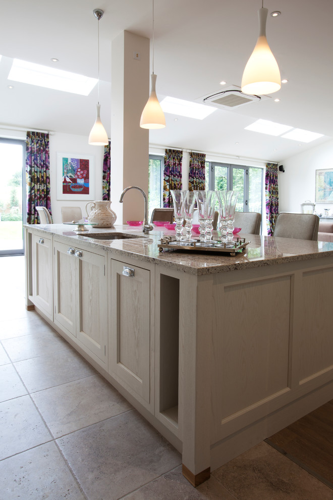 This is an example of a large traditional galley eat-in kitchen in London with an undermount sink, shaker cabinets, white cabinets, granite benchtops, white splashback, glass sheet splashback, stainless steel appliances, travertine floors and with island.