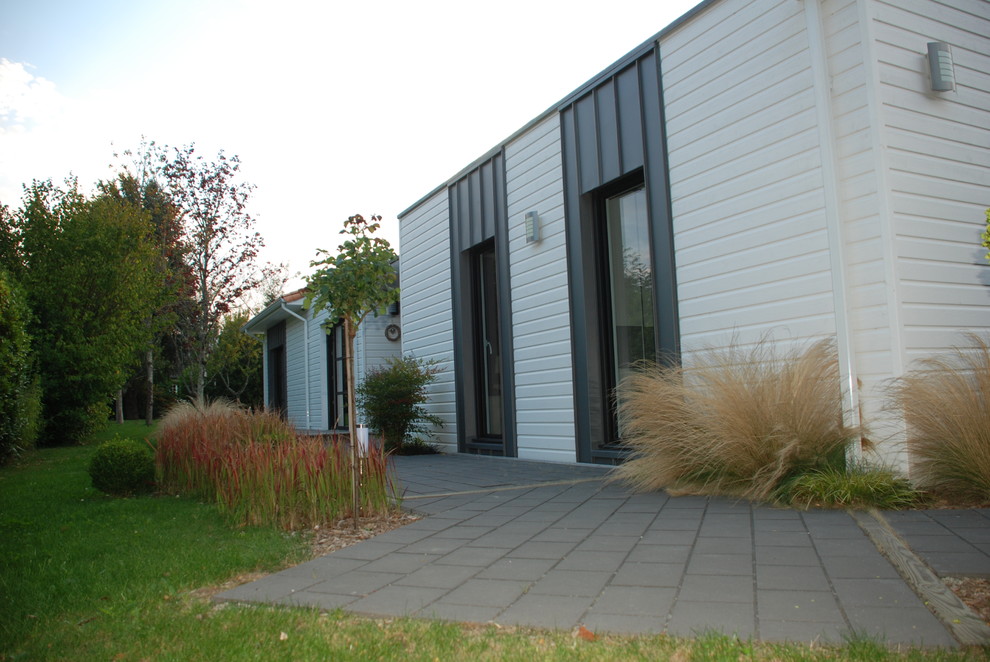 This is an example of a contemporary one-storey white exterior in Nantes with wood siding and a hip roof.
