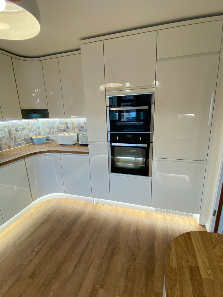 Photo of a large modern u-shaped separate kitchen in Other with an undermount sink, recessed-panel cabinets, white cabinets, laminate benchtops, multi-coloured splashback, ceramic splashback, black appliances, vinyl floors, no island, multi-coloured floor and multi-coloured benchtop.
