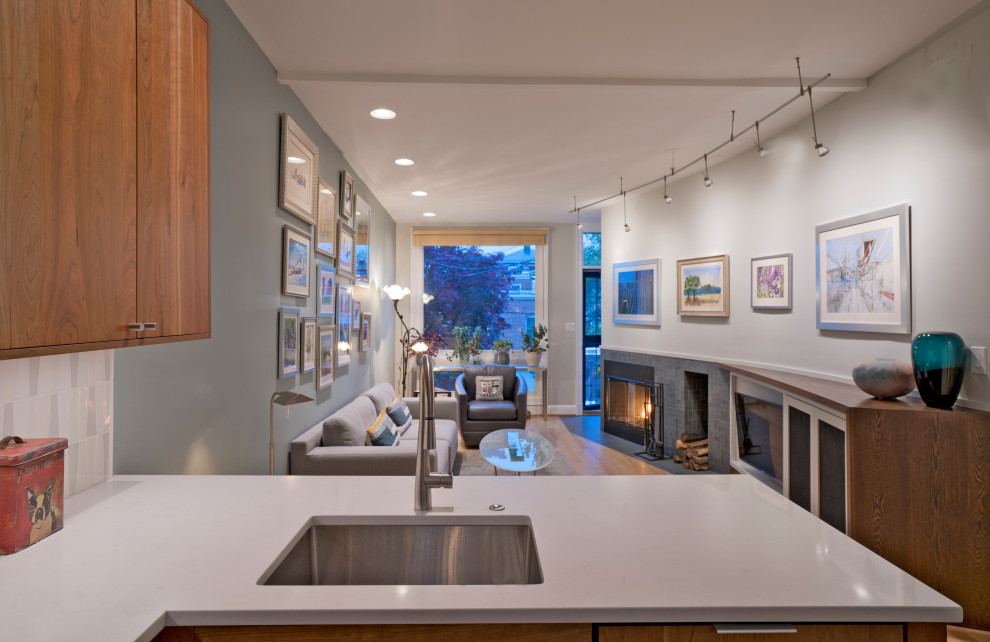 This is an example of a mid-sized midcentury u-shaped open plan kitchen in DC Metro with light hardwood floors, beige floor, an undermount sink, flat-panel cabinets, medium wood cabinets, quartz benchtops, white splashback, ceramic splashback, panelled appliances, a peninsula, white benchtop and vaulted.