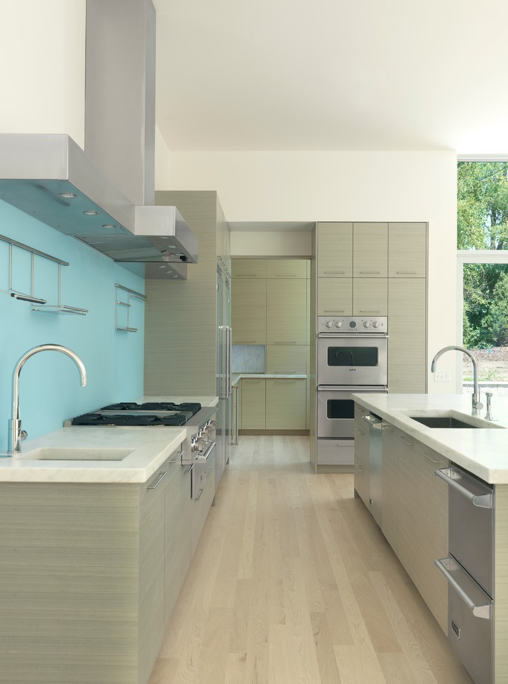 Inspiration for a mid-sized modern galley open plan kitchen in St Louis with stainless steel appliances, an undermount sink, flat-panel cabinets, light wood cabinets, marble benchtops, blue splashback, glass sheet splashback, light hardwood floors and with island.