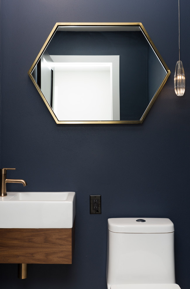 This is an example of a small modern powder room in Milwaukee with flat-panel cabinets, brown cabinets, a one-piece toilet, blue walls, porcelain floors, a wall-mount sink, solid surface benchtops and white floor.