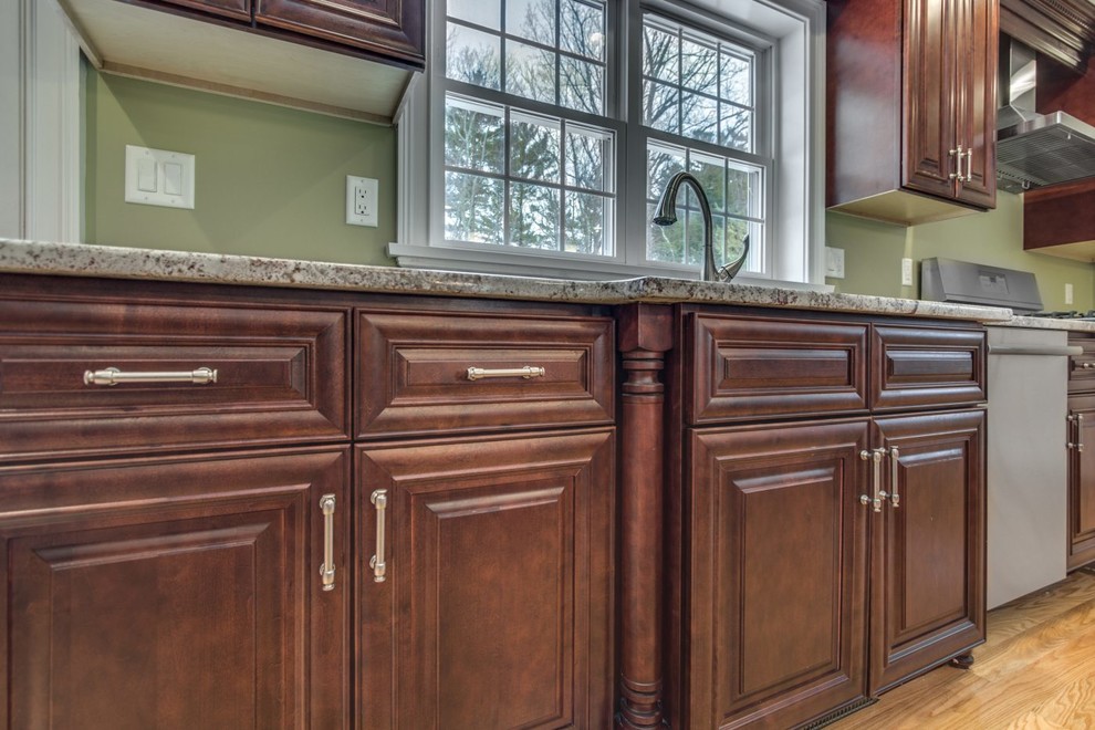 Inspiration for a mid-sized traditional eat-in kitchen in Raleigh with an undermount sink, raised-panel cabinets, medium wood cabinets, granite benchtops, stainless steel appliances, light hardwood floors, with island, yellow floor and beige benchtop.