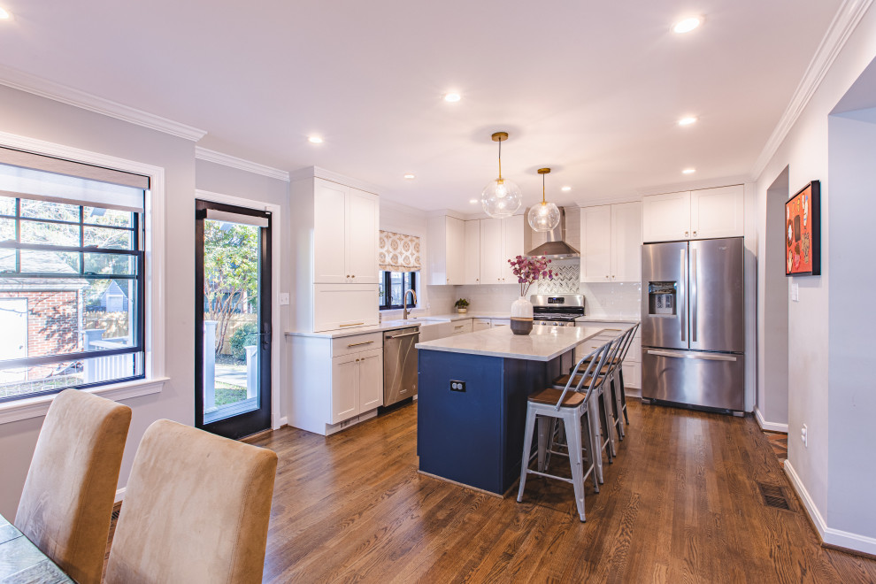 Example of a mid-sized transitional l-shaped medium tone wood floor and brown floor eat-in kitchen design in DC Metro with a farmhouse sink, shaker cabinets, white cabinets, quartzite countertops, white backsplash, subway tile backsplash, stainless steel appliances, an island and gray countertops