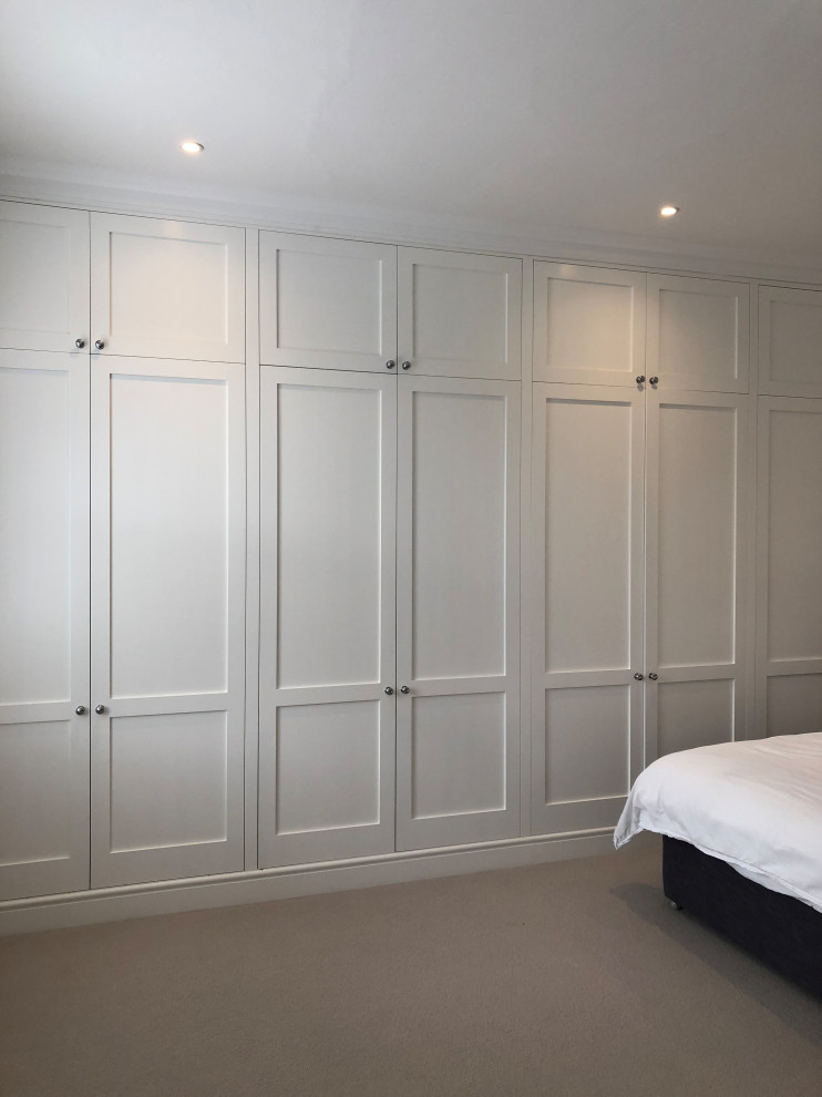 Expansive traditional storage and wardrobe in London with recessed-panel cabinets, white cabinets, carpet and beige floor.