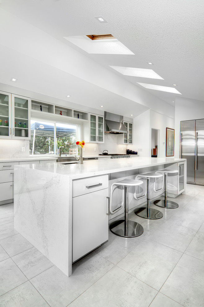 This is an example of a large contemporary l-shaped kitchen in San Diego with an undermount sink, glass-front cabinets, white cabinets, white splashback, stainless steel appliances, with island, marble benchtops, stone slab splashback, marble floors and white floor.