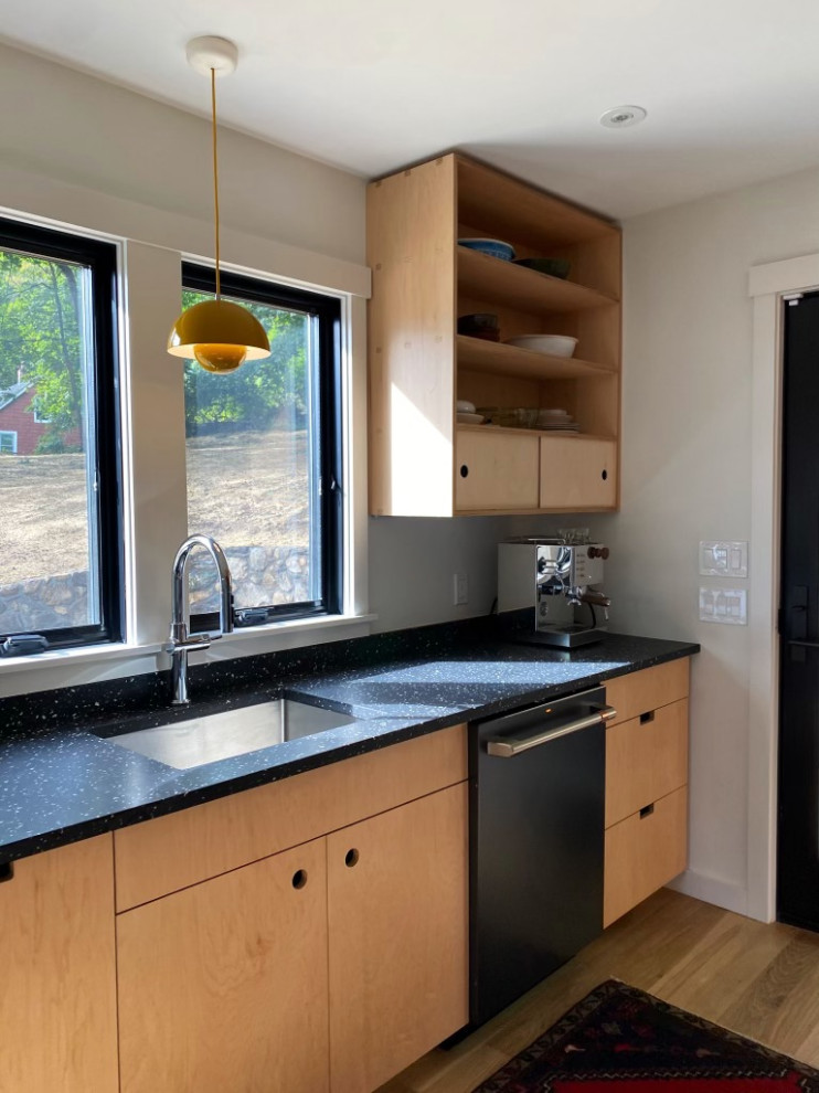 Foto di una piccola cucina parallela minimalista con lavello sottopiano, ante lisce, ante in legno chiaro, top alla veneziana, paraspruzzi nero, elettrodomestici neri, parquet chiaro e top nero
