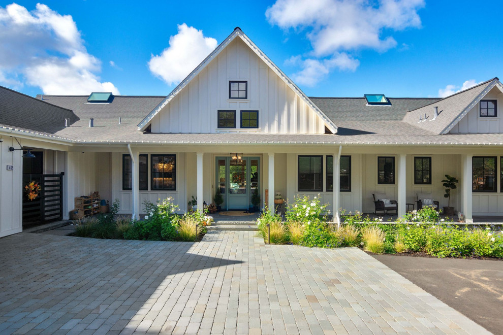 Foto della villa grande bianca country a un piano con rivestimento in legno, tetto a capanna, copertura a scandole, tetto grigio e pannelli e listelle di legno