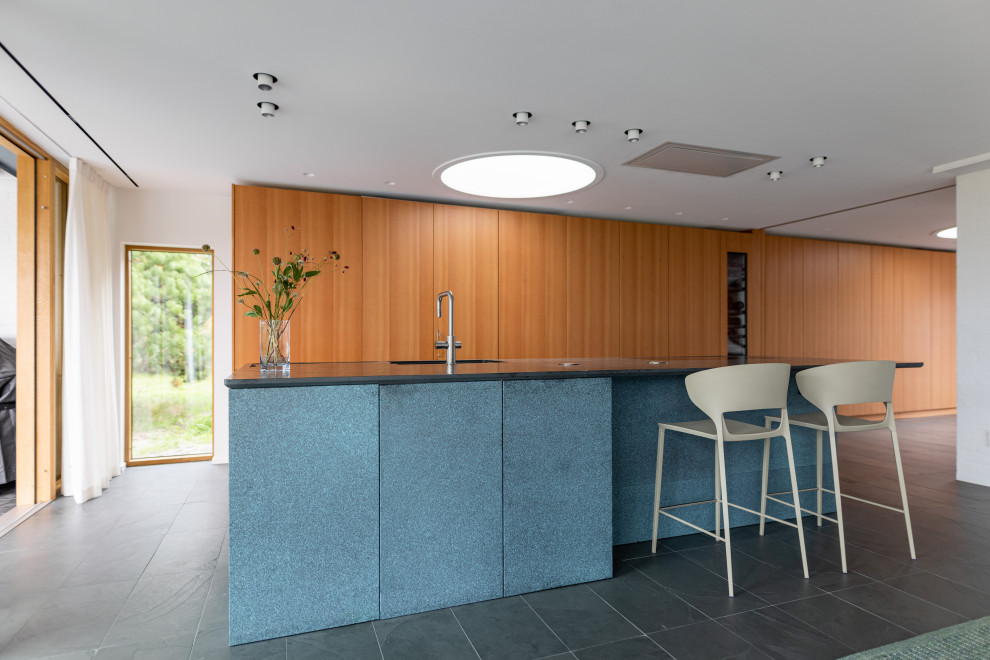 This is an example of a large modern galley open plan kitchen in Malmo with an undermount sink, flat-panel cabinets, medium wood cabinets, copper benchtops, panelled appliances, slate floors, with island, grey floor and turquoise benchtop.