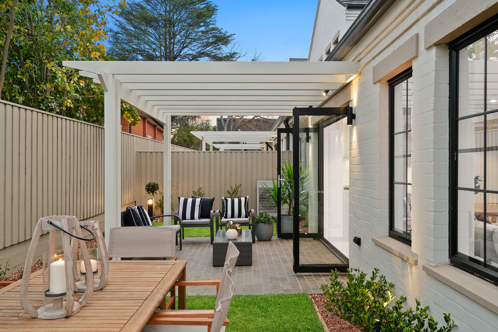 Design ideas for a small transitional backyard patio in Sydney with natural stone pavers and a pergola.