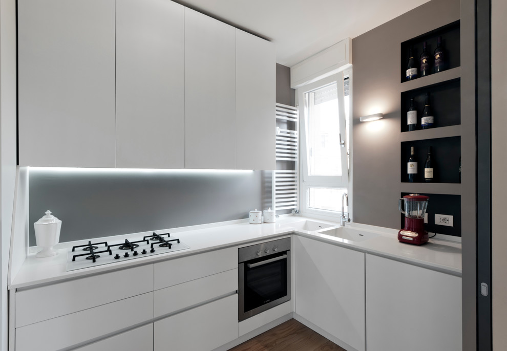 Large modern u-shaped separate kitchen in Milan with an integrated sink, flat-panel cabinets, white cabinets, solid surface benchtops, grey splashback, stainless steel appliances, light hardwood floors and no island.