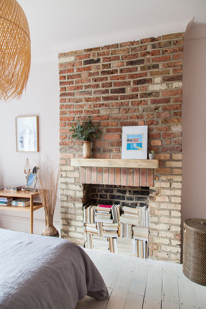 Design ideas for a mid-sized eclectic master bedroom in London with pink walls, painted wood floors, a standard fireplace, a brick fireplace surround and white floor.